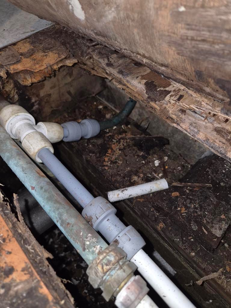 Plastic and copper pipework beneath a suspended timber floor.